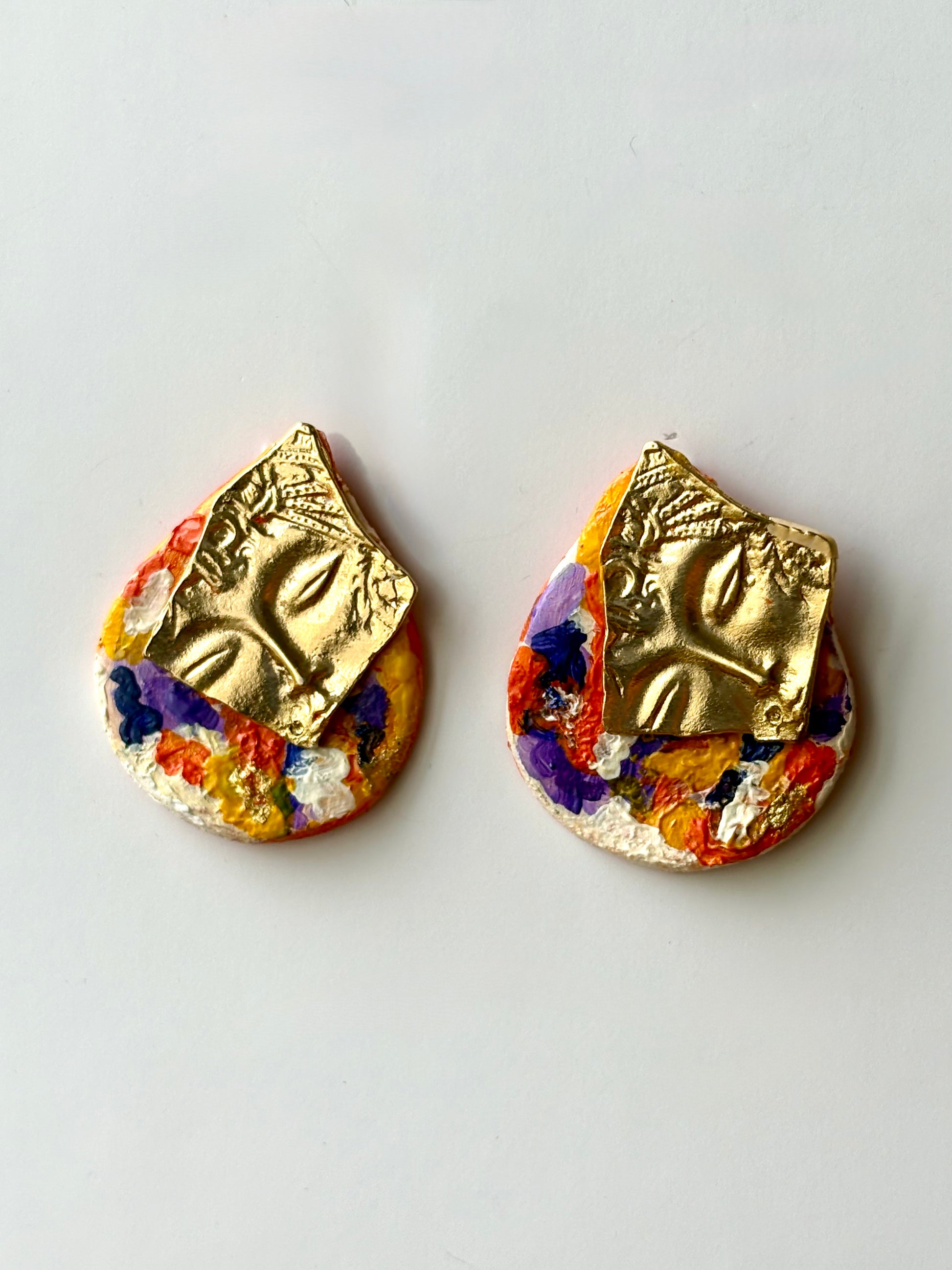 Handcrafted colorful painted stud earrings featuring an embossed gold metal face plate on a white background