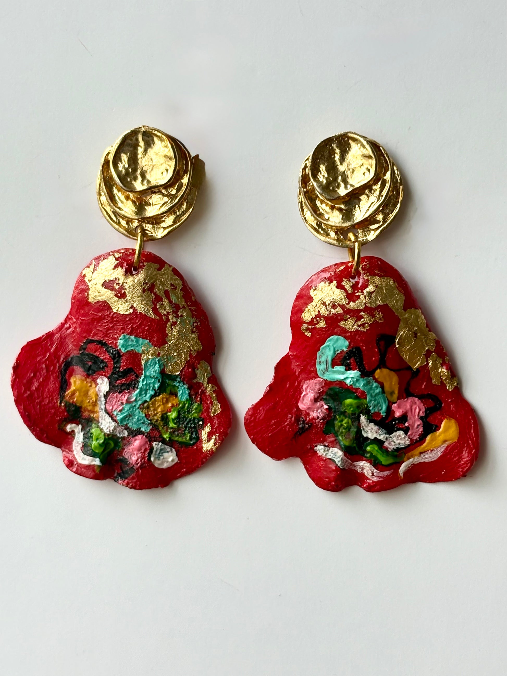 Bright red handcrafted drop earrings with gold foil accents and textured gold studs on a white background