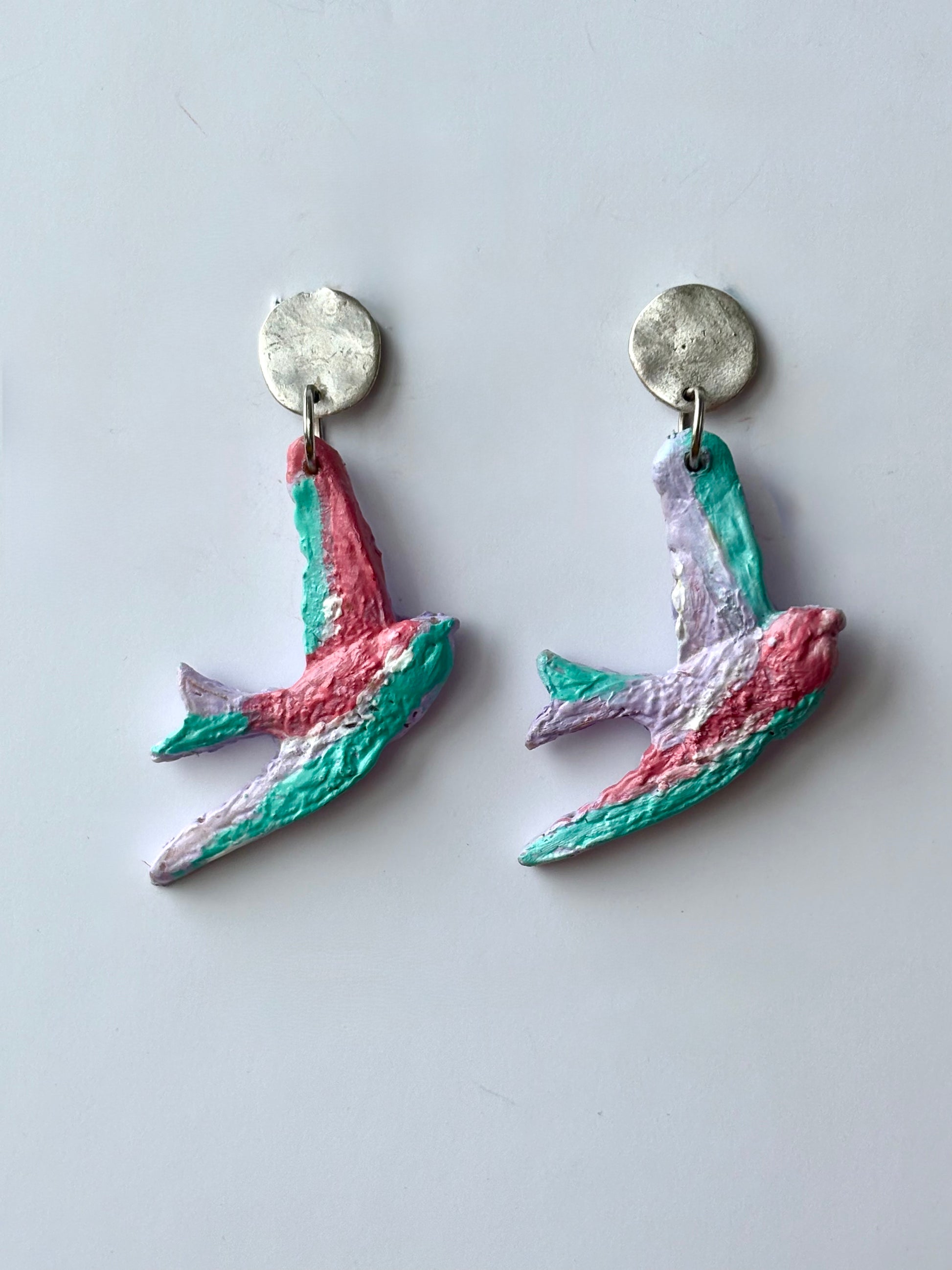 Handmade and hand-painted pastel bird dangle earrings with silver metallic studs on a white background