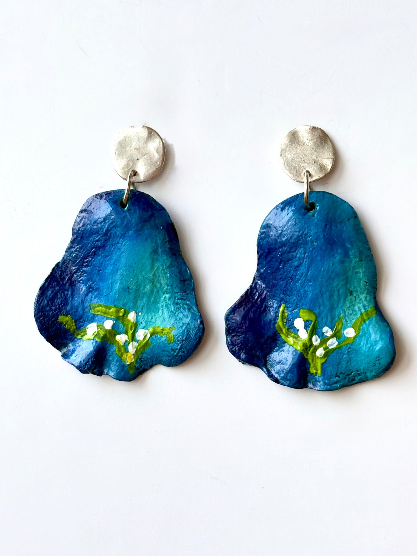 Handmade and hand-painted blue floral drop earrings with silver metallic studs on a white background