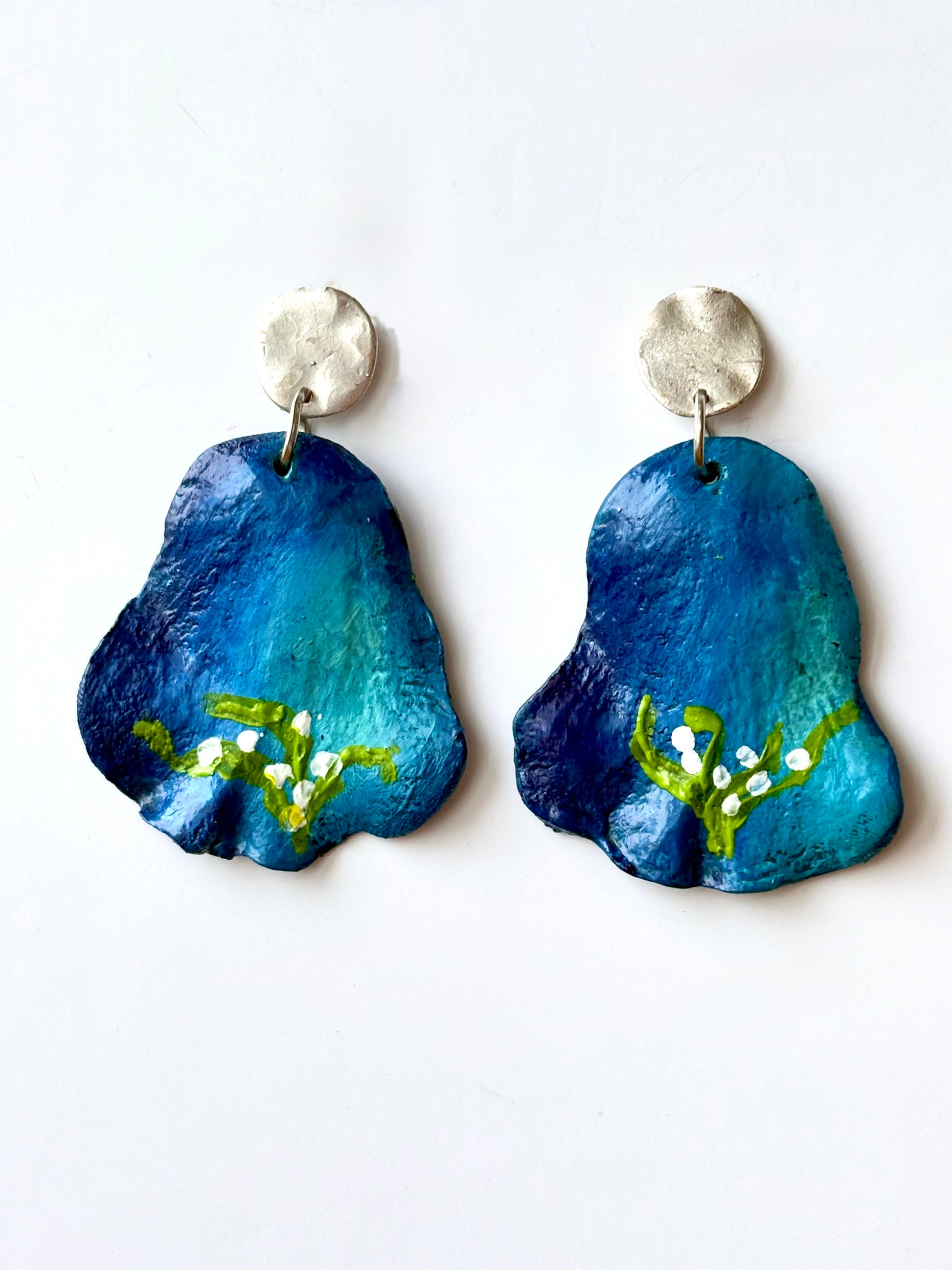 Handmade and hand-painted blue floral drop earrings with silver metallic studs on a white background