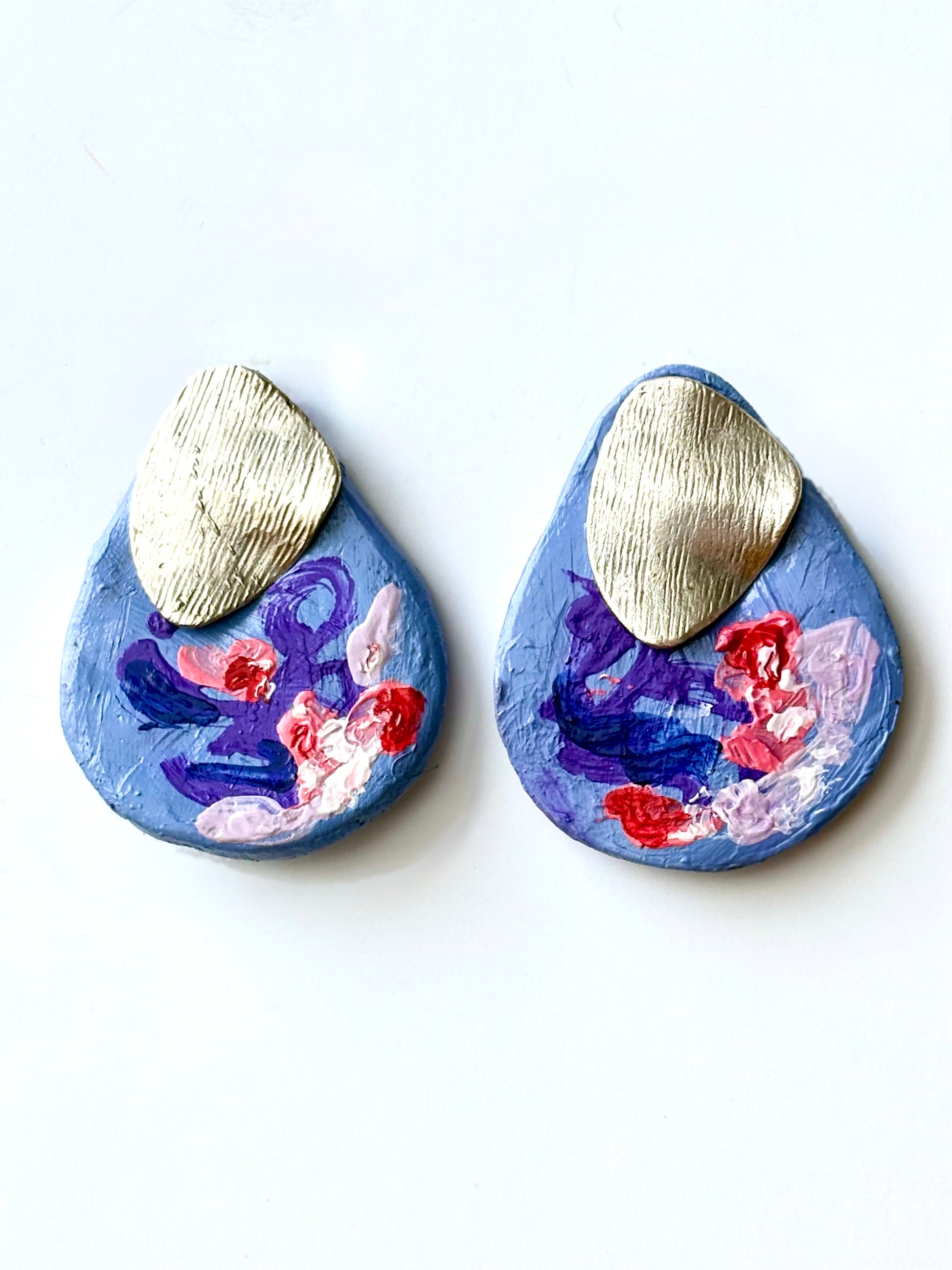 Handmade and hand-painted periwinkle stud earrings with textured gold metal accent plates on a white background