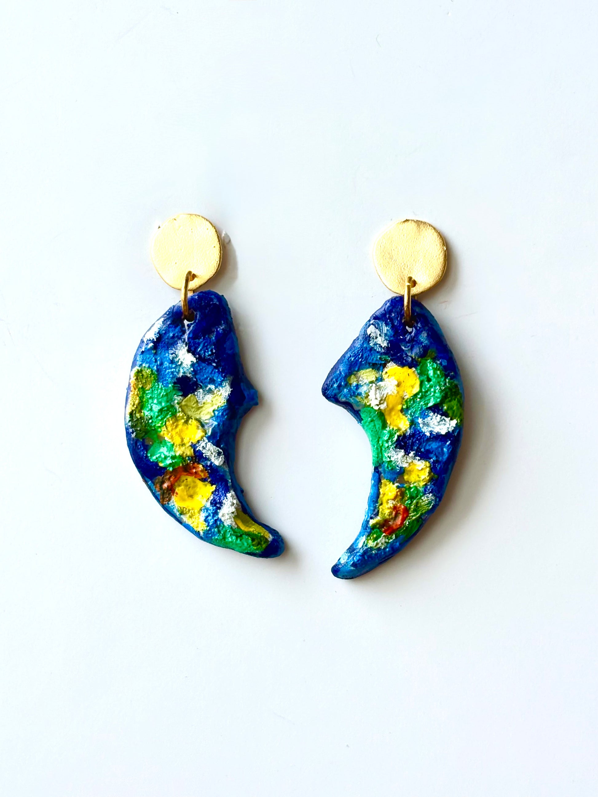 Handmade and hand-painted blue and yellow crescent dangle earrings with gold studs on a white background