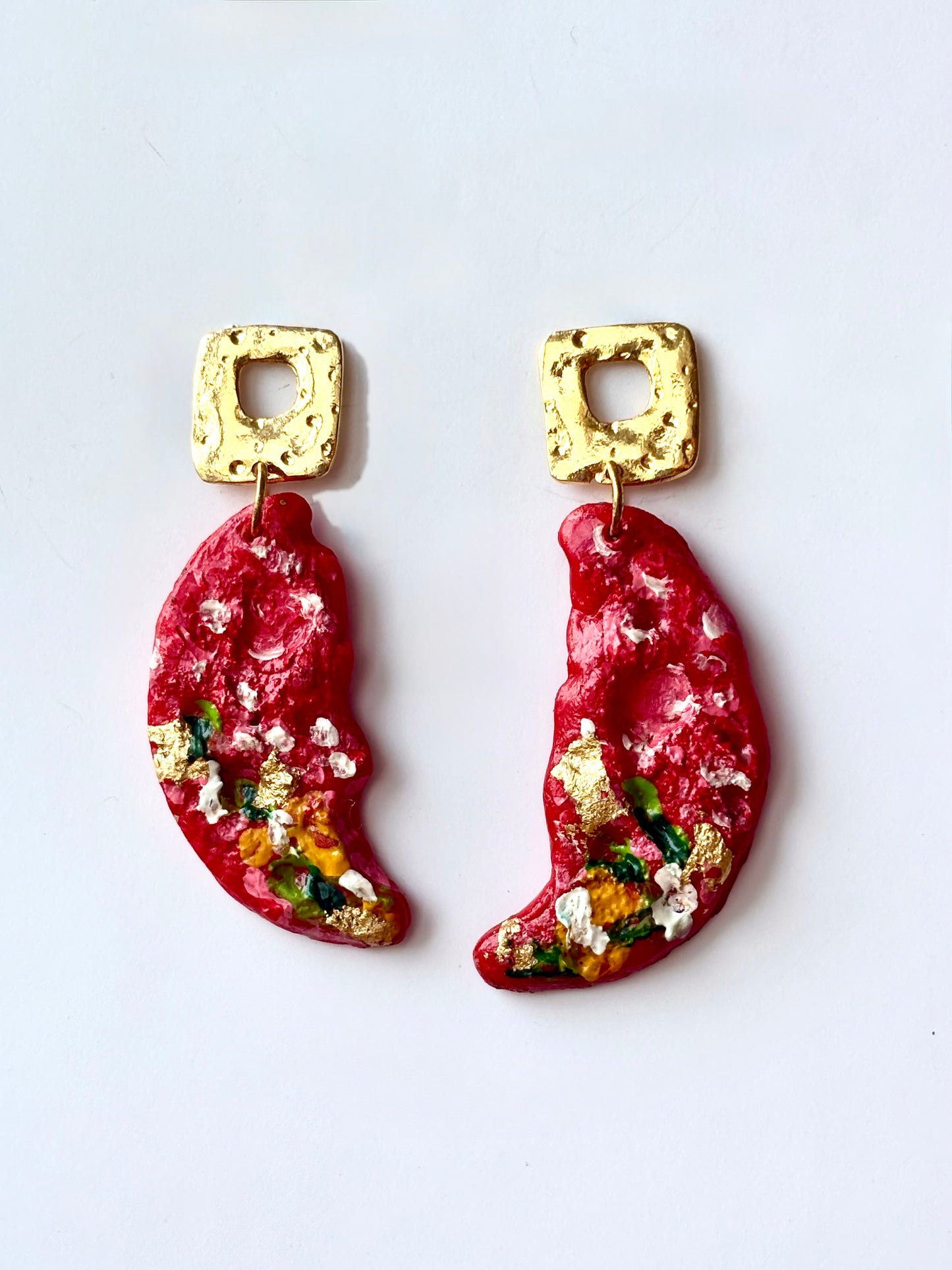 Handmade and hand-painted bright red crescent dangle earrings with gold leaf details and square gold studs on a white background